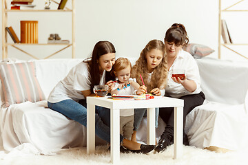 Image showing Little girls, attractive young mother and charming grandmother are sitting at home