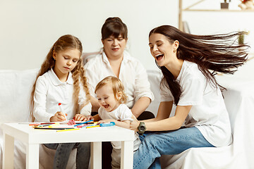 Image showing Little girls, attractive young mother and charming grandmother are sitting at home