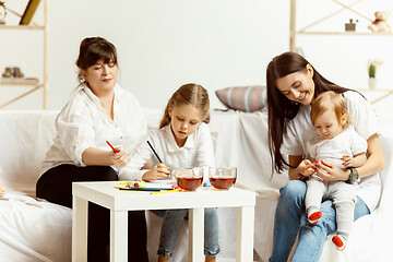 Image showing Little girls, attractive young mother and charming grandmother are sitting at home