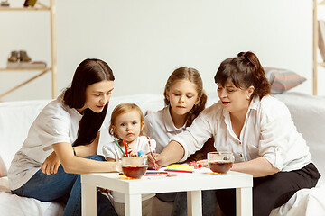 Image showing Little girls, attractive young mother and charming grandmother are sitting at home