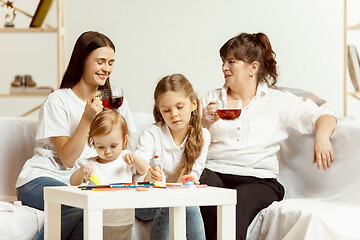 Image showing Little girls, attractive young mother and charming grandmother are sitting at home