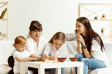 Image showing Little girls, attractive young mother and charming grandmother are sitting at home