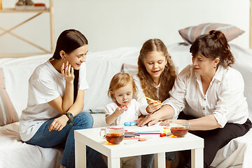 Image showing Little girls, attractive young mother and charming grandmother are sitting at home