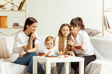 Image showing Little girls, attractive young mother and charming grandmother are sitting at home