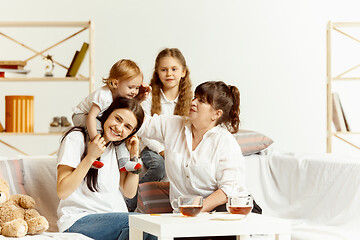 Image showing Little girls, attractive young mother and charming grandmother are sitting at home