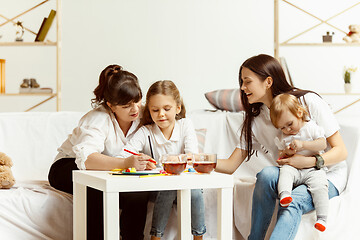 Image showing Little girls, attractive young mother and charming grandmother are sitting at home