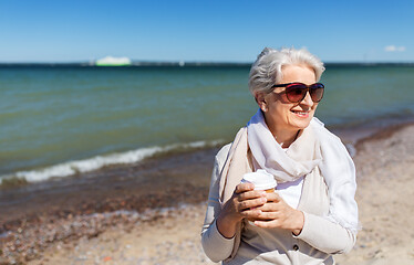 Image showing senior woman drinking takeaway coffee on beach