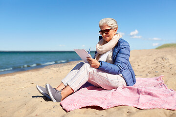 Image showing senior woman writing to notebook on summer beach