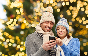 Image showing happy couple with smartphone over christmas lights