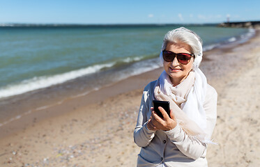 Image showing old woman in headphones with smartphone on beach