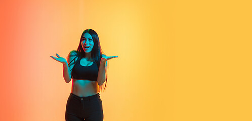 Image showing Young woman\'s portrait on yellow-orange studio background in neon light