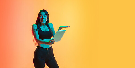Image showing Young woman\'s portrait on yellow-orange studio background in neon light