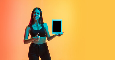 Image showing Young woman\'s portrait on yellow-orange studio background in neon light