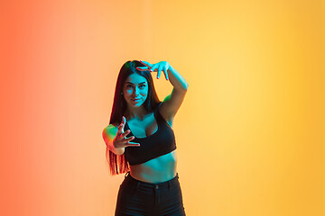 Image showing Young woman\'s portrait on yellow-orange studio background in neon light