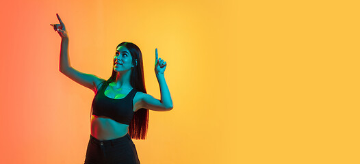 Image showing Young woman\'s portrait on yellow-orange studio background in neon light