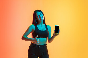 Image showing Young woman\'s portrait on yellow-orange studio background in neon light