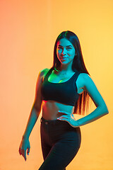 Image showing Young woman\'s portrait on yellow-orange studio background in neon light