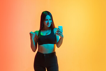 Image showing Young woman\'s portrait on yellow-orange studio background in neon light