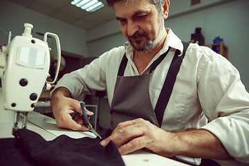 Image showing Sewing process of the leather belt. Old Man\'s hands behind sewing.