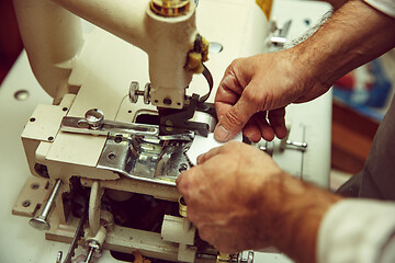 Image showing Sewing process of the leather belt. old Man\'s hands behind sewing.