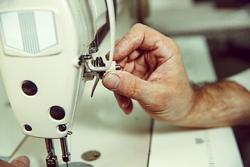 Image showing Sewing process of the leather belt. old Man\'s hands behind sewing.