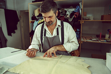 Image showing Closeup of tailors table with male hands tracing fabric making pattern for clothes