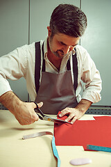 Image showing Closeup of tailors table with male hands tracing fabric making pattern for clothes