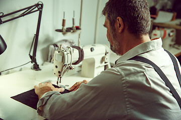 Image showing Sewing process of the leather belt. old Man\'s hands behind sewing.