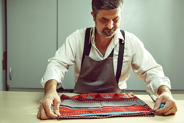 Image showing Closeup of tailors table with male hands tracing fabric making pattern for clothes