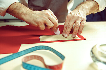 Image showing Closeup of tailors table with male hands tracing fabric making pattern for clothes