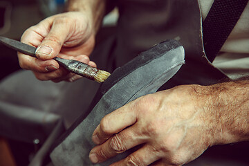 Image showing Shoemaker makes shoes for men.He smears special liquid with a brush.