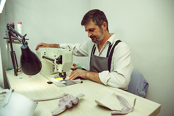 Image showing Sewing process of the leather belt. old Man\'s hands behind sewing.