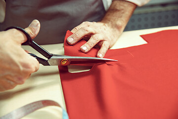 Image showing Closeup of tailors table with male hands tracing fabric making pattern for clothes