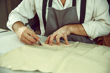 Image showing Closeup of tailors table with male hands tracing fabric making pattern for clothes