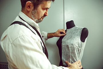 Image showing Closeup of tailors table with male hands tracing fabric making pattern for clothes