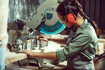 Image showing Busy and serious craftswoman grinding timbers with special machine.