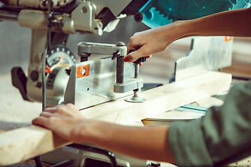 Image showing Busy and serious craftswoman grinding timbers with special machine.