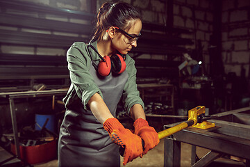 Image showing Busy and serious craftswoman grinding timbers with special machine.