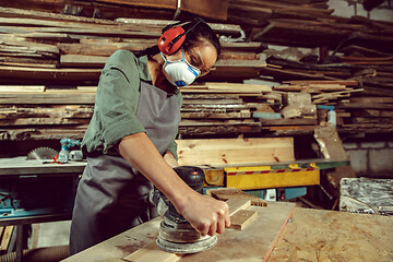 Image showing Busy and serious craftswoman grinding timbers with special machine.