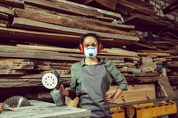 Image showing Busy and serious craftswoman grinding timbers with special machine.