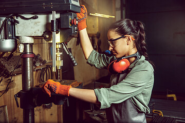 Image showing Busy and serious craftswoman grinding timbers with special machine.