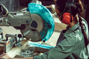 Image showing Busy and serious craftswoman grinding timbers with special machine.