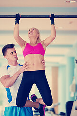 Image showing trainer support young woman while lifting on bar in fitness gym