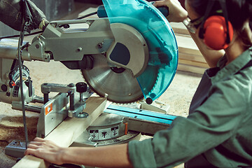 Image showing Busy and serious craftswoman grinding timbers with special machine.