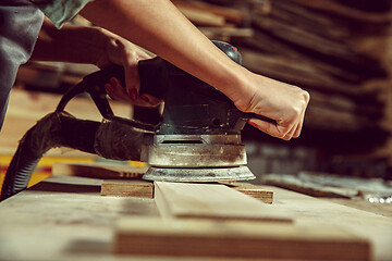 Image showing Hands of craftswoman grinding timbers with special machine.