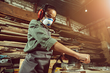 Image showing Busy and serious craftswoman grinding timbers with special machine.