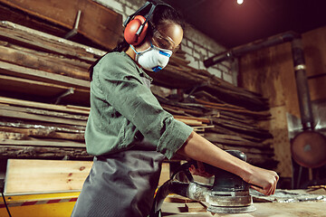 Image showing Busy and serious craftswoman grinding timbers with special machine.