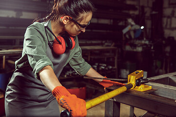 Image showing Busy and serious craftswoman grinding timbers with special machine.