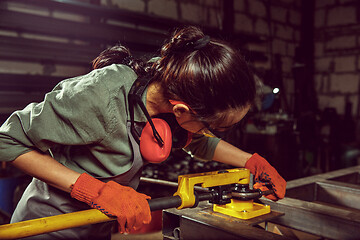 Image showing Busy and serious craftswoman grinding timbers with special machine.