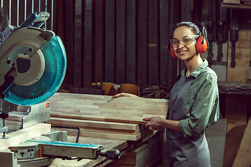 Image showing Smiling craftswoman grinding timbers with special machine.